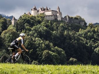 Cyclist in front of a densely wooded hill with a castle