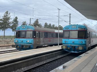 Zwei blau-graue CP-Regionalzüge an einem Bahnsteig in Vila Real de Santo António, Algarve. Oberleitungen und Bäume sichtbar.