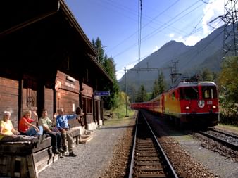 Reisende am Bergbahnhof Stugl/Stuls mit Zug auf dem Nachbargleis