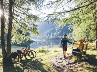 Cyclists take a break on a bench by a mountain lake.