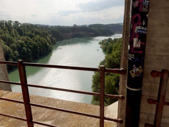 Blick vom Grandfey-Viadukt auf einen gewundenen Fluss durch bewaldetes Tal mit grünem Wasser, Betongeländer und Brückenstruktur sichtbar.