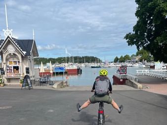 Eine Fahrradfahrerin fährt mit ausgestreckten Beinen auf den Hafen von Naantali, Finnland zu. Viele Schiffe stehen auf dem Wasser.