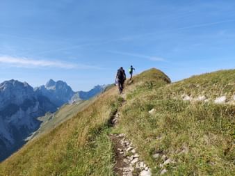 Zwei Wanderer auf einem schmalen Bergkamm-Wanderweg am Marwees im Alpstein, mit dramatischen Alpengipfeln im Hintergrund.