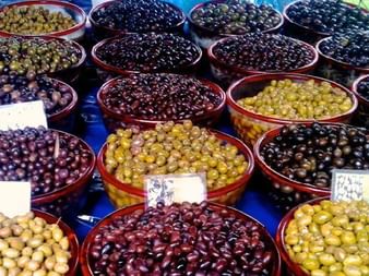 Marktstand mit verschiedenen Oliven in roten Schalen auf Korfu. Grüne, gelbe, violette und schwarze Oliven in Reihen mit Preisschildern.