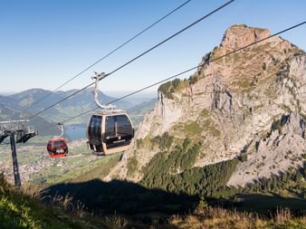 Cable car gondolas ascending over rocky mountain peak near Rothenfluh with Lake Lucerne and green valleys visible in the background.