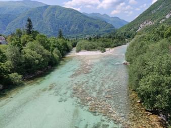 Breiter türkisfarbener Fluss Soca in Slowenien. Umgeben von viel Bäumen und bewaldeten Bergen.