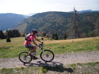 Trailrunnerin fährt gemütlich mit ihrem Bike. Im Hintergrund eine schöne Wiesenlandschaft und Waldhügel.