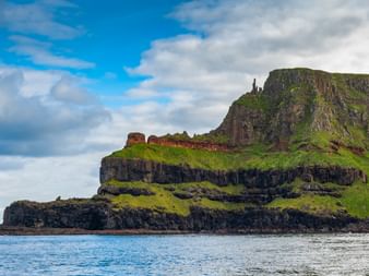 Dramatische geschichtete Basaltklippen mit grünem Gras, die aus blauen Küstengewässern bei Carrick-a-Rede in County Antrim, Nordirland, aufragen.