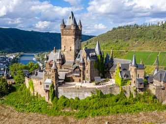 Blick auf die Reichsburg Cochem, umgeben von Weinbergen und dem Ort, mit der Mosel im Hintergrund