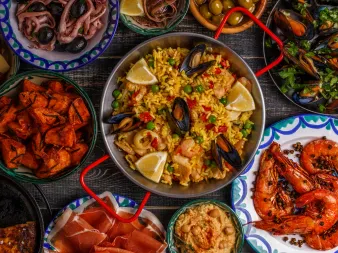 Aufsicht auf spanische Gerichte: Paella mit Muscheln und Zitrone, gegrillte Garnelen, Chorizo, Oliven, Schinken und Meeresfrüchte.