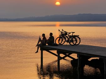 Deux vététistes, assis avec leurs vélos, sur le ponton, devant un magnifique coucher de soleil.