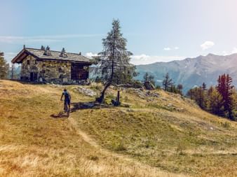 Ein Mountainbiker fährt auf ein altes Steinhaus zu, das oben auf einem Berghügel steht.