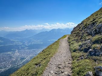 Schotterweg auf der Hafelekarspitze mit Panoramablick auf das Innsbrucker Tal und das Karwendelgebirge unter blauem Himmel.