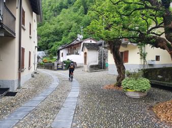 Eine Velofahrerin fährt durch das Dorf Maggia im Tessin.