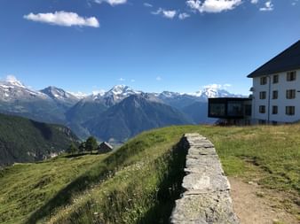 Steinmauer mit Haus mit Bergpanorama im Hintergrund.