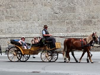 Traditionelle Pferdekutsche mit Fahrgästen in Salzburg. Zwei braune Pferde ziehen eine gelbe Holzkutsche mit Kutscher in Hut und Weste.