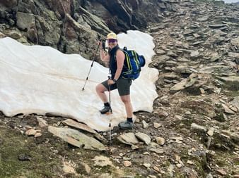 Ein Wanderer geht über ein Schneefeld mit felsigem Untergrund