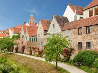 Historisches Donauwörth an der Romantischen Straße Mittelalterliche Stadt Donauwörth mit traditionellen deutschen Häusern, roten Ziegeldächern und Kirchturm. Bunte Blumen blühen am Flussuferweg.