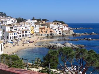 Malerisches Küstendorf in Nordkatalonien mit bunten mediterranen Häusern entlang eines Sandstrandes und felsiger Küste.