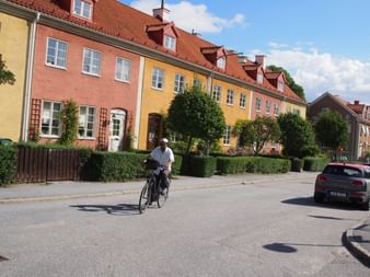Radfahrer auf einer ruhigen Straße in Stockholm mit bunten Reihenhäusern in Gelb und Rosa mit roten Ziegeldächern und gepflegten Hecken.