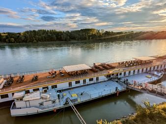 Flusskreuzfahrtschiff MS Prinzessin Katharina am Steg in Bratislava bei Sonnenuntergang. Das weiße Schiff mit Holzdeck liegt an der Donau.