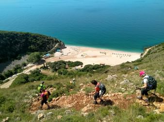 Wanderer steigen einen felsigen Pfad hinab mit Blick auf einen Sandstrand mit türkisfarbenem Wasser in Himare, Albanien.