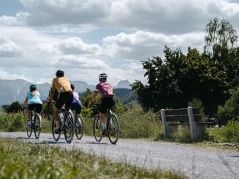Vier Radfahrer auf Gravelbikes auf einem Weg im Naturpark Gantrisch bei Bern, mit Bergen und bewölktem Himmel im Hintergrund.