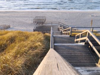 Eine Holztreppe führt hinab auf einen Sandstrand an der Nordsee.