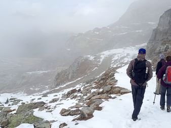 Srei Wanderer laufen uf dem Schnee auf bewölkten Bergen.