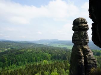Hohe Barbarine Felssäule am Pfaffenstein mit Blick auf weite bewaldete Landschaft und entfernte Hügel unter bewölktem Himmel.