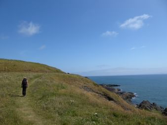 Eine Person wandert an der Küste Schottlands durch weitläufige Graslandschaften.