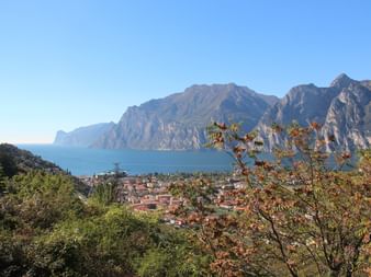 Panoramablick auf den Gardasee mit Riva del Garda zwischen dramatischen Bergen und blauem Seewasser unter klarem Himmel.