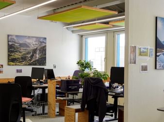 Moderner Büroraum mit mehreren Arbeitsplätzen, schwarzen Bürostühlen, Computern und Berglandschaftsfotos an weißen Wänden.