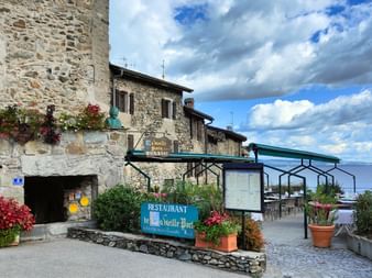 Restaurant en pierre avec enseignes bleues du Vieille Port à Yvoire, terrasse extérieure donnant sur le lac Léman sous ciel nuageux.