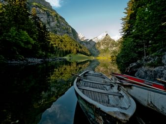 Holzruderboote am Ufer des Seealpsees mit perfekten Bergspiegelungen. Schneebedeckte Alpengipfel und grüne Wälder rahmen das ruhige Wasser ein.