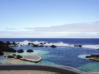 Natürliche Schwimmbecken mit türkisfarbenem Wasser und Vulkanfelsen an Madeiras Küste, mit Meereswellen und blauem Himmel im Hintergrund.