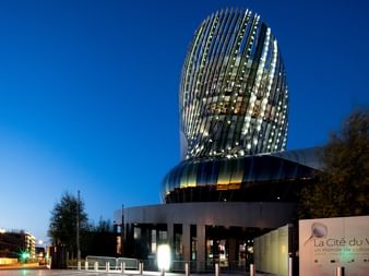 Le musée du vin La Cité du Vin à Bordeaux au crépuscule, avec sa tour dorée distinctive aux panneaux de verre incurvés sur fond de ciel bleu.