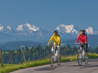 Zwei Radfahrer fahren durch Affoltern im Emmental mit Blick auf die Alpen.