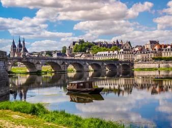 Steinbrücke mit mehreren Bögen über die Loire in Blois, mit gotischen Kathedraltürmen und historischen Gebäuden im ruhigen Wasser gespiegelt.