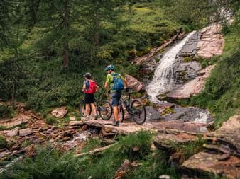 Velofahrer überqueren einen Bach. Gottardo-Bike. Veloferien mit Eurotrek.