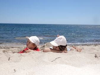 Zwei Kinder mit Käppi sind im Sand eingebudelt.