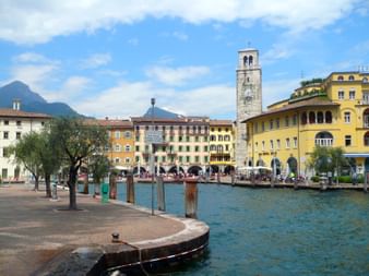 Steinerner Anleger in Riva erstreckt sich ins türkisfarbene Wasser mit bunten Gebäuden und hohem mittelalterlichem Uhrenturm im Hintergrund.