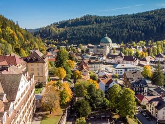 Luftaufnahme von St. Blasien mit seiner markanten Kuppelkirche, umgeben von bunten Herbstbäumen und bewaldeten Hügeln im Schwarzwald.
