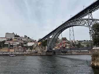 Die ikonische Ponte Luis I Eisenbogenbrücke über den Douro in Porto, mit bunten Häusern am Hang und bewölktem Himmel.
