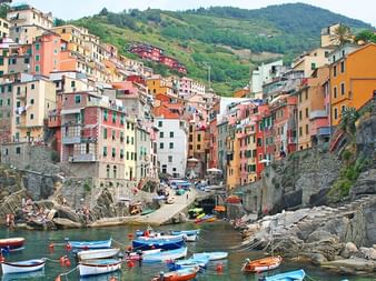 Riomaggiore-Dorf mit bunten Häusern auf Klippen über einem kleinen Hafen voller Fischerboote und felsiger Küste.