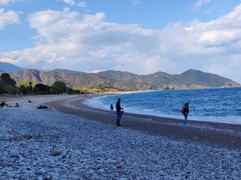 Ein Steinstrand in der Türkei mit Bergen und Wäldern im Hintergrund.