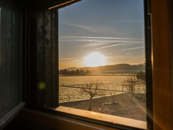 Blick durch ein Planwagenfenster in Courtedoux, Jura Ajoie, mit Sonnenaufgang über frostbedeckten Feldern mit kahlen Bäumen und fernen Hügeln.