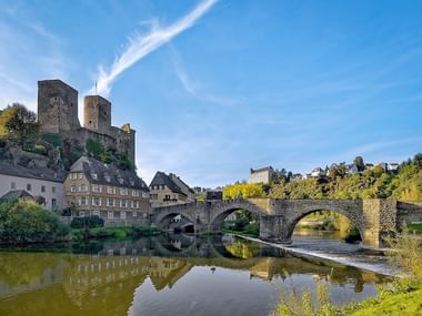 Mittelalterliche Türme der Burg Runkel auf Hügel über Steinbrücke der Lahn, mit historischen Gebäuden und perfekten Wasserspiegelungen.