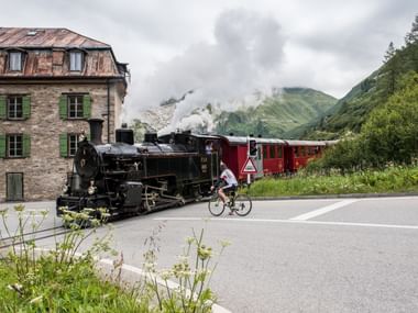 Die Furka-Bahn mit ihrer alten, schwarzen Lokomotive fährt durch ein Dorf.