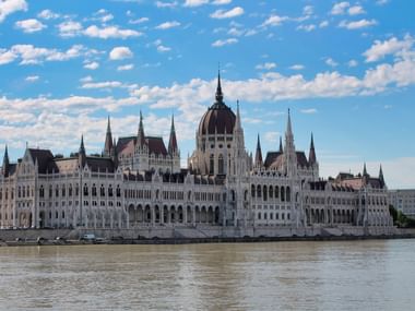 Das ungarische Parlamentsgebäude in Budapest von der anderen Seite der Donau aus gesehen, mit neugotischer Architektur und zentraler Kuppel.